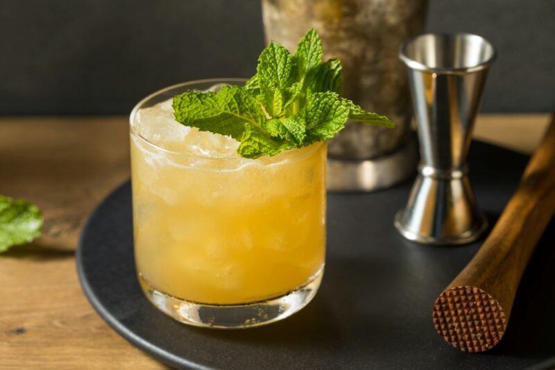 A smash Firebapple cocktail with peppermint leaves on a black tray next to a cocktail jigger