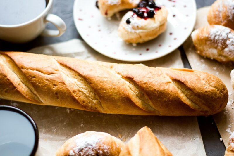 A French baguette on a wooden table, with plates of treats nearby