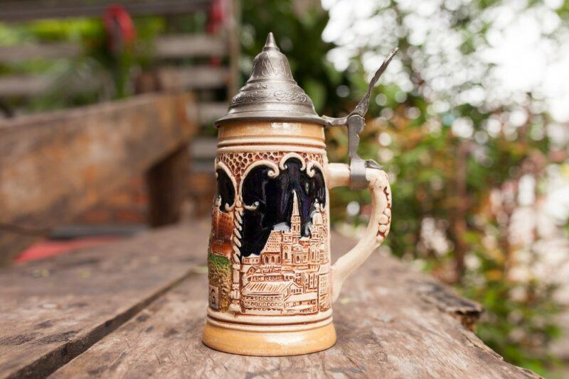 A single German beer stein sitting on a wooden step, with a pewter lid and beautiful illustrations