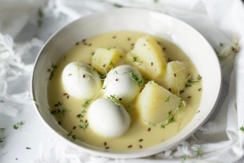 A German egg and potato dish called senfeier that is in a white bowl with a mustard sauce