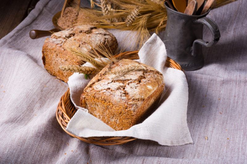 Several loaves of rustic German bread, where one is in a basket with a white cloth