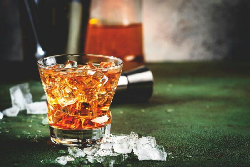 A glass containing a Godfather cocktail with plenty of ice on a green table