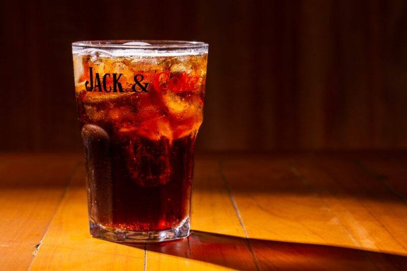 A tall Jack and Coke cocktail in a glass, where the glass itself has Jack and Coke written on it.