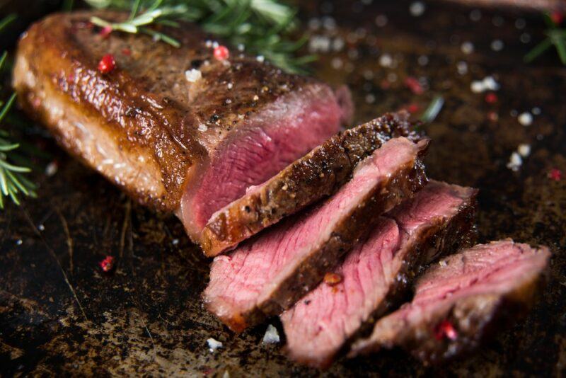 A wooden table with a cooked piece of New York strip steak that has been slieced