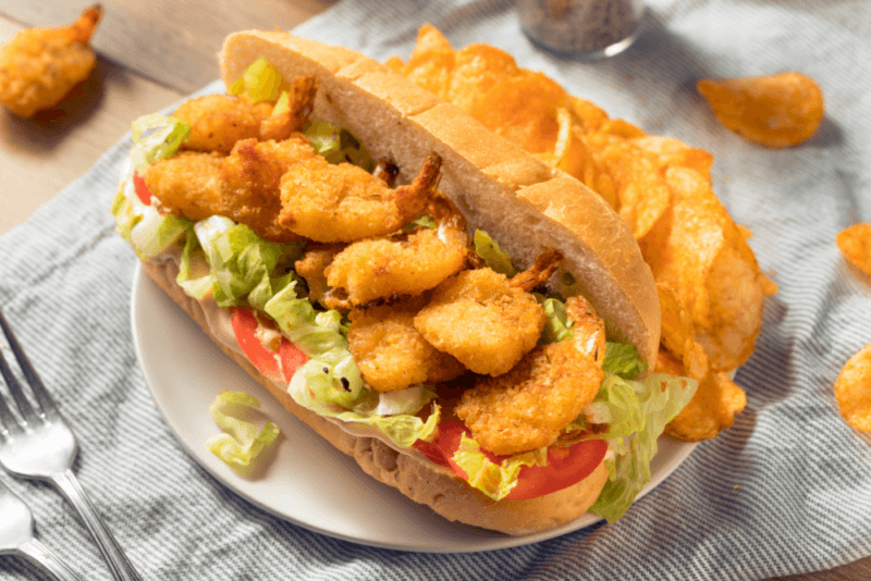 A large Po'boy sandwich with plenty of lettuce, tomatoes, and prawns, on a white plate.