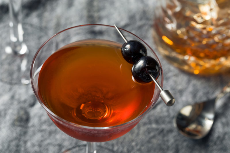 A red Rob Roy cocktail in a glass with two olives