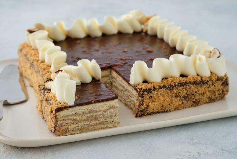 A large white plate containing a Russian dessert called Leningradsky cake, with cream around the edges