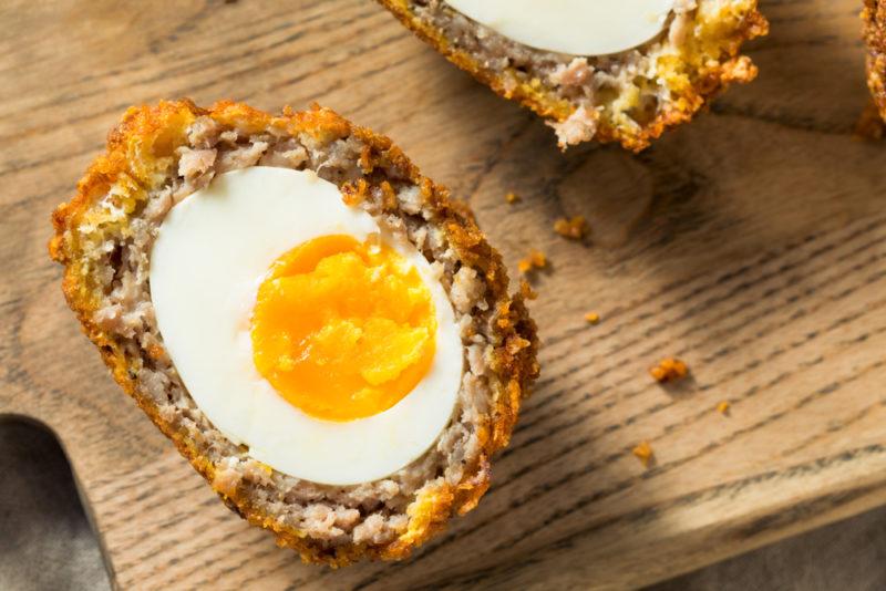 A Scotch egg that has been sliced in half on a wooden board