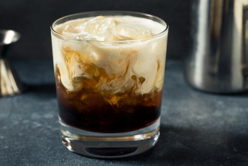 A white Russian cocktail in a glass on a gray table, next to some cocktail tools