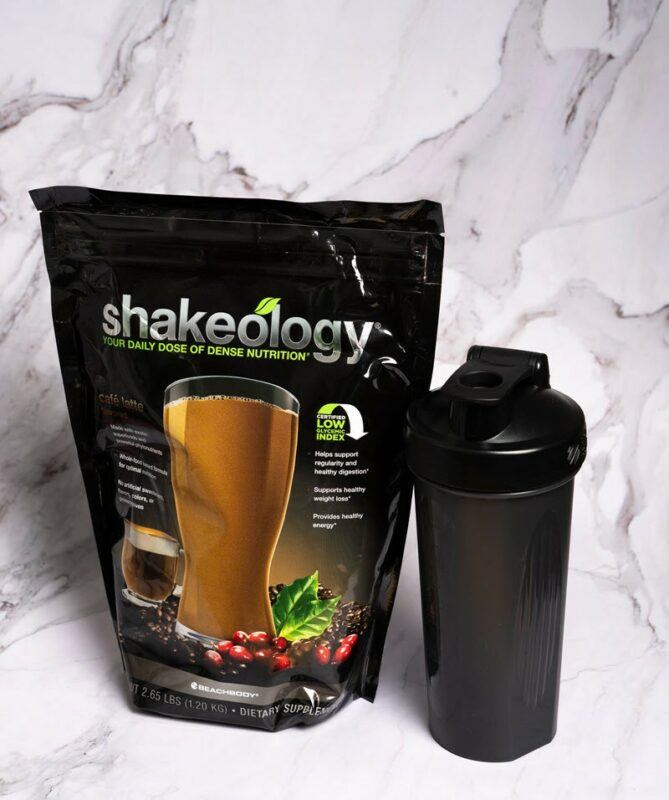 A bag of Shakeology protein powder, next to a black shaker