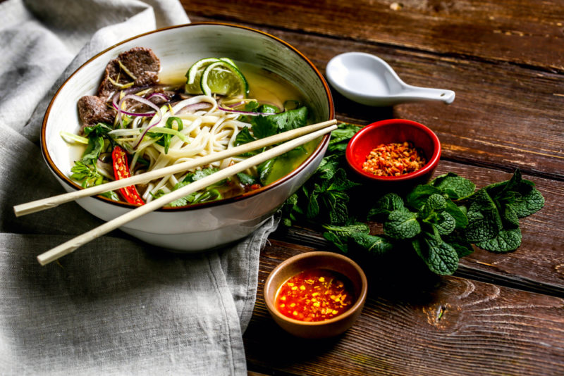 A bowl full of a Taiwanese meal with chopsticks and two small dishes of sauce