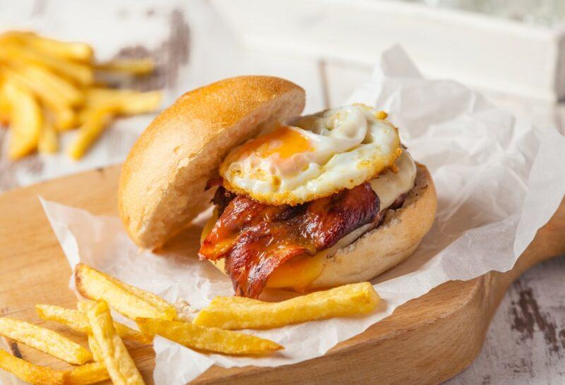 A homemade burger with bacon and eggs, next to potato fries