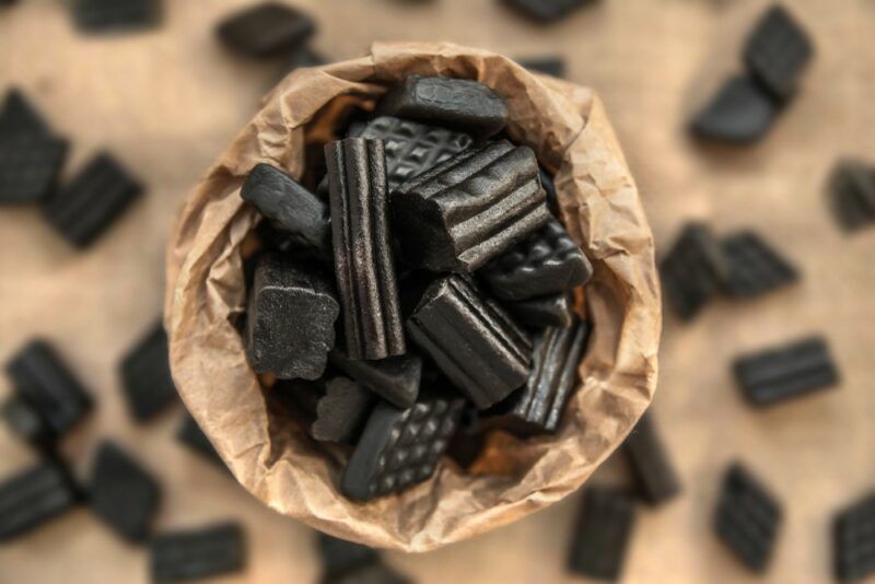 A brown paper bag filled with black licorice, with more licorice scattered across the table