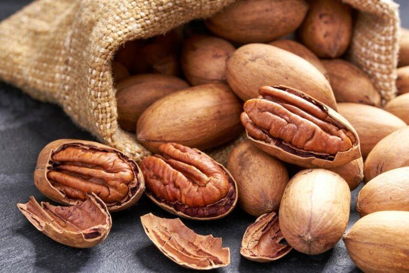 A brown bag filled with pecans, some of which have their shells open