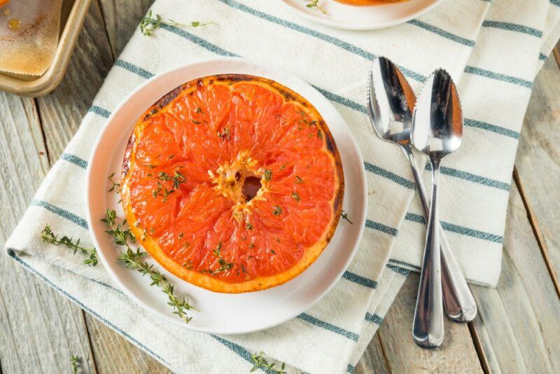 A white plate with baked grapefruit next to two spoons