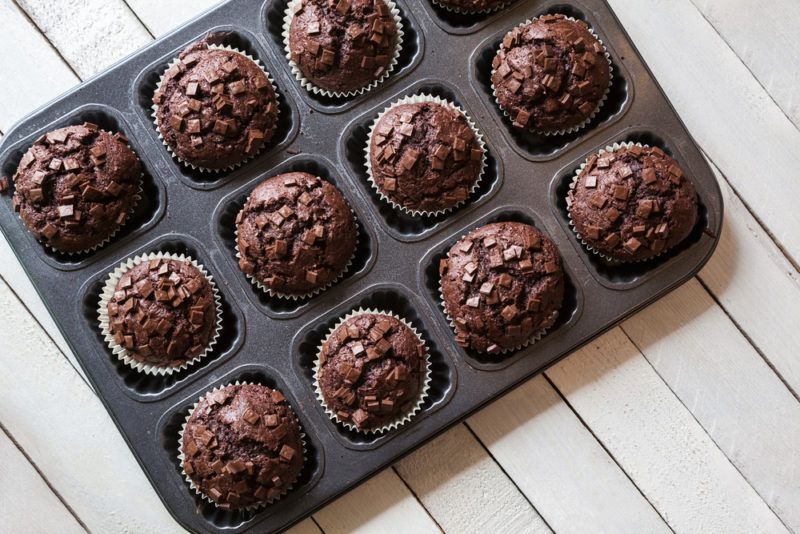 A muffin tray that contains a dozen freshly baked chocolate chip muffins on a wooden table or deck