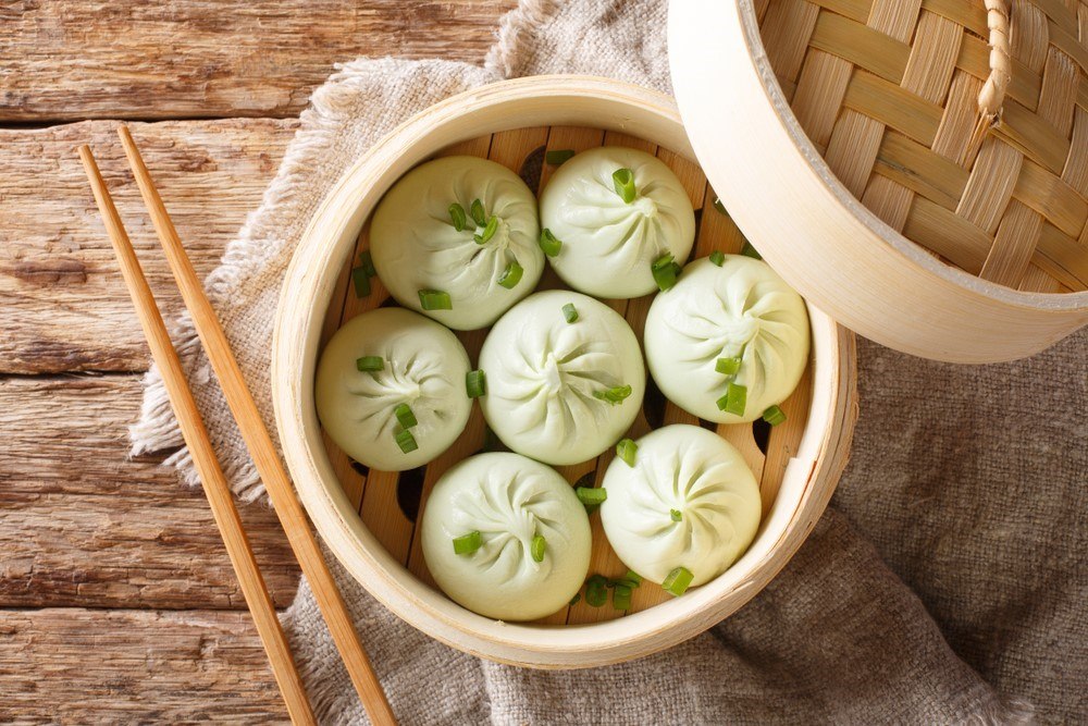 A bamboo steamer with 7 steamed buns, next to chopsticks