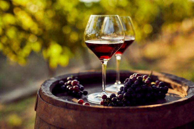 A barrel with two glasses of red wine, with a few bunches of grapes