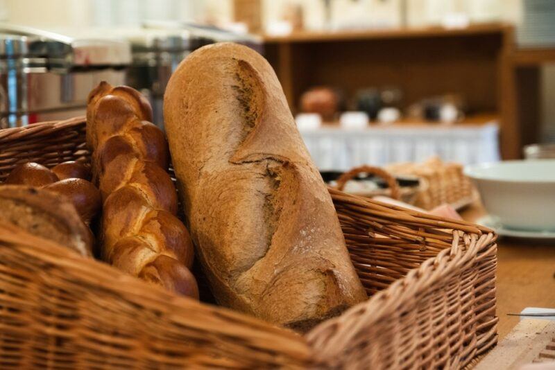 A basket containing two large loaves of bread, plus some smaller pieces of bread. There's an out of focus bakery in the background.