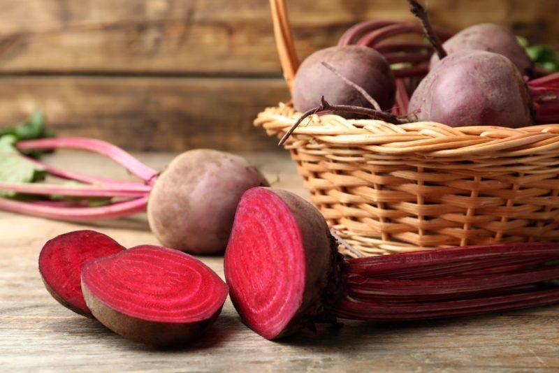 A basket filled with beets, next to a whole beet and one that has been sliced