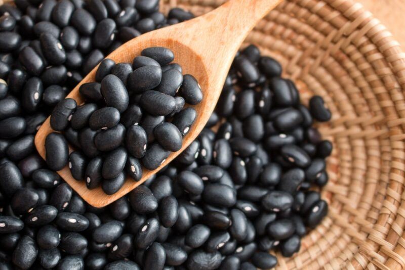 A basket filled with black beans, where a wooden spoon is being used to scoop some of the beans