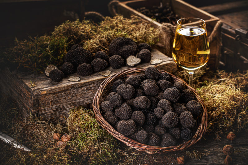 A large basket of truffles next to a glass of wine and a selection of truffles