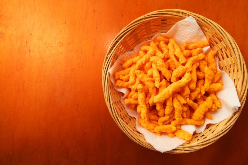 A basket of cheese curls on a light wooden table