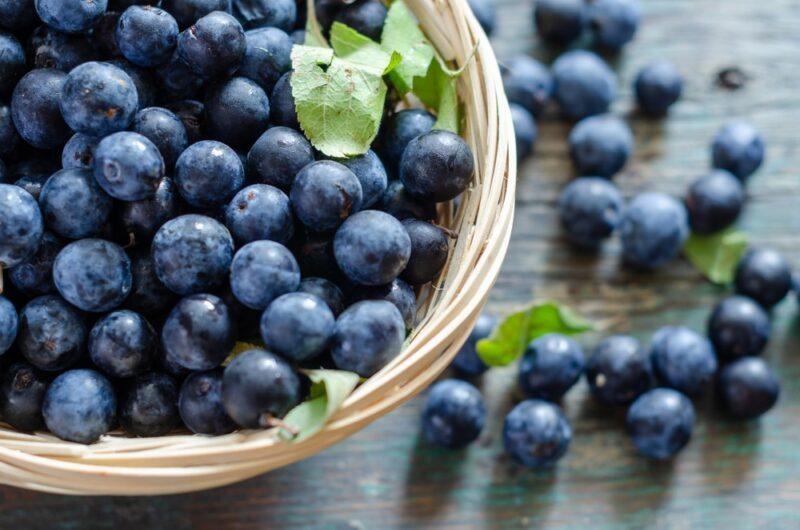 A basket of fresh blueberries, with more blueberries scattered on the table