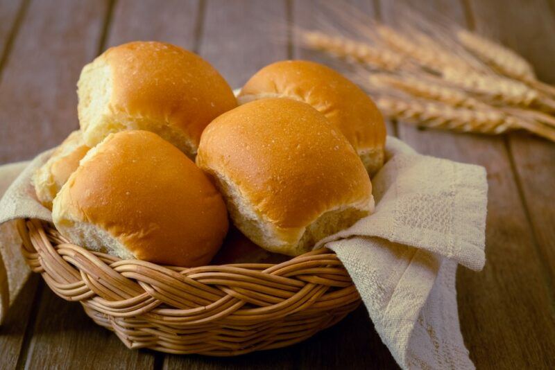 A wooden table with a basket and a collection of fresh bread rolls