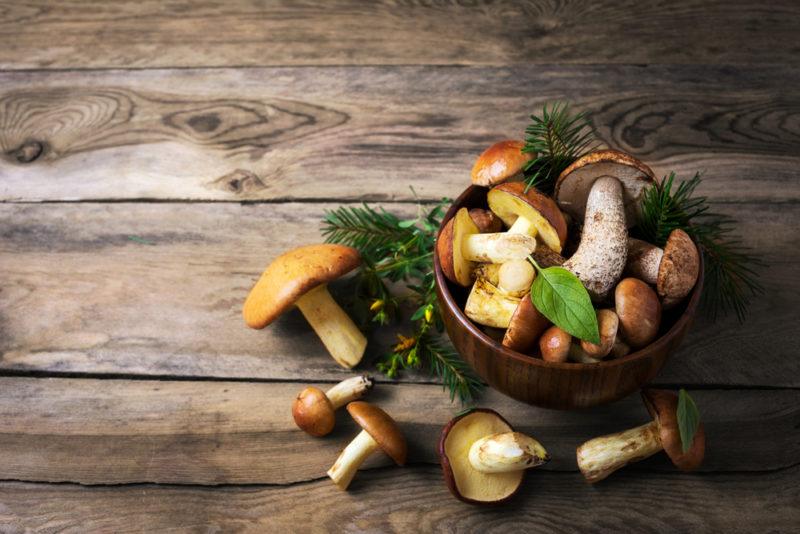 A brown basket with fresh mushrooms and a few more mushrooms on a wooden table