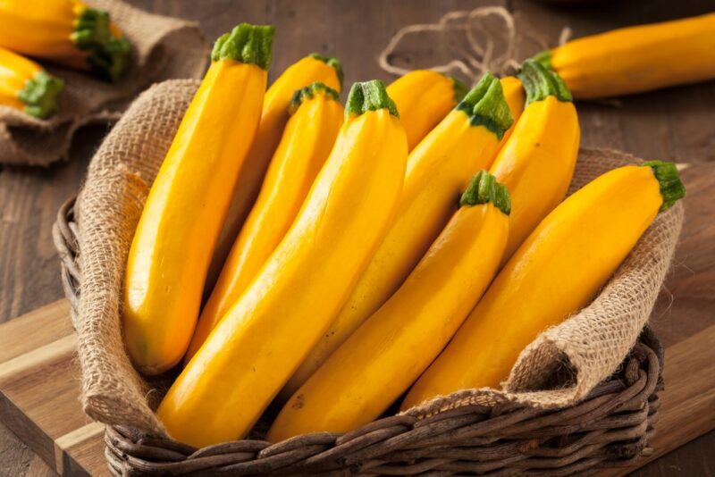 A basket with a cloth that contains a large number of yellow squash, also called yellow zucchini