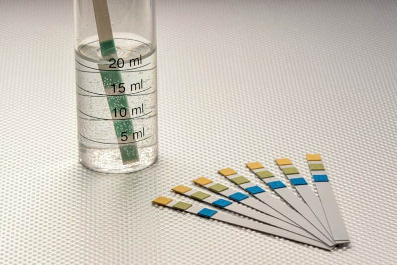 A fan of pH test strips, next to a beaker with a test stips in it