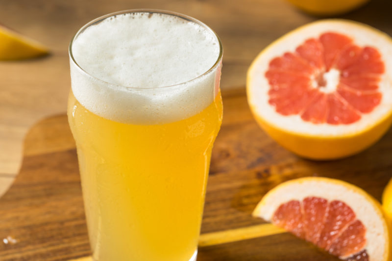 A pint glass containing shandy, next to a half grapefruit and a piece of grapefruit