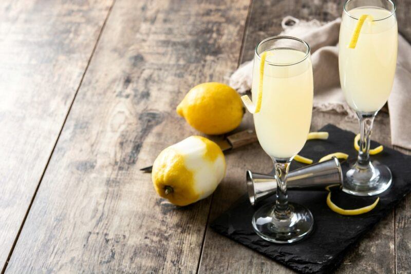 Two glasses of a tall bee's nice cocktail, next to some lemons on a wooden table