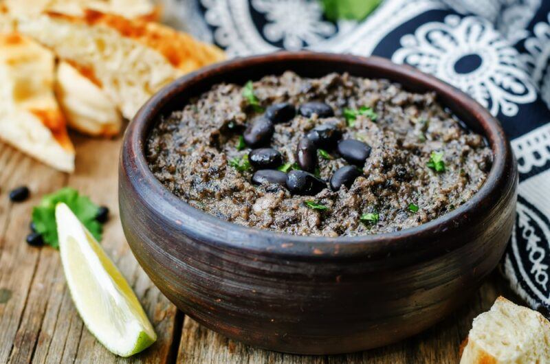 A black bowl filled with black bean hummus, with a few of the beans on the top