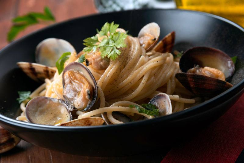 A black bowl with cooked clams and pasta