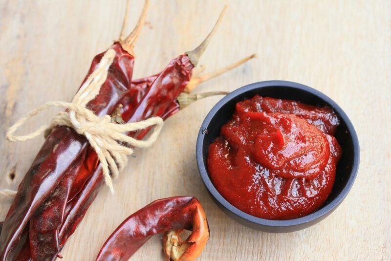 A light blue bowl of hot sauce, next to some hot peppers on a wooden table