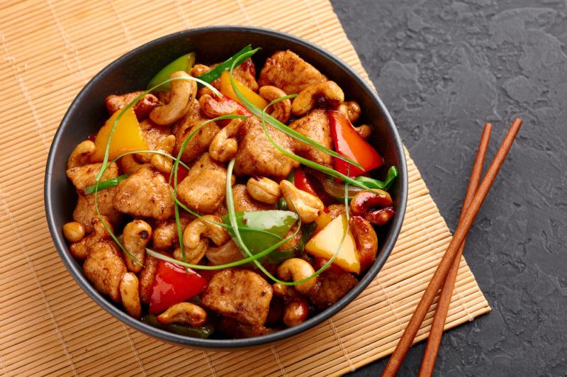 A black bowl of kai pad med ma muang next to chopsticks. The disk includes stir fried chicken and cashews