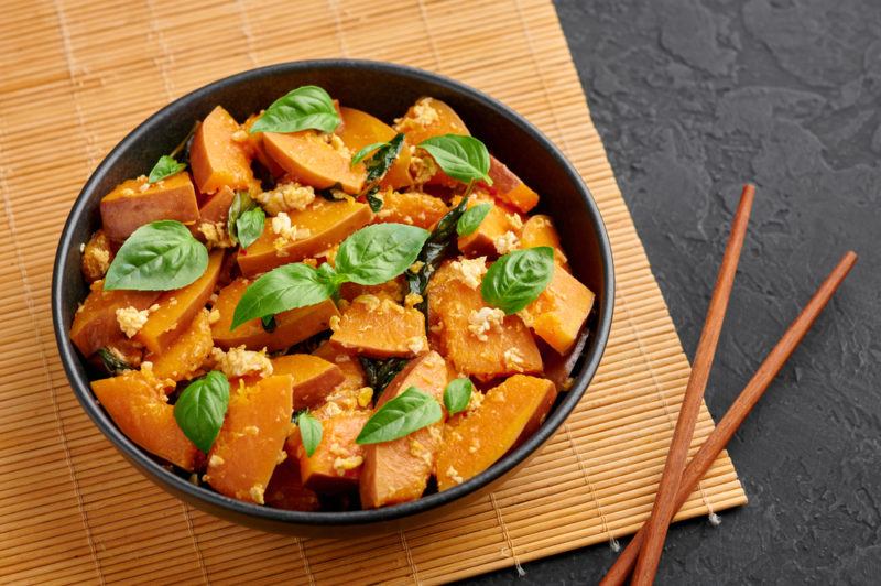 A black bowl of pad phuk tong next to chopsticks. The dish includes pumpkin and greens