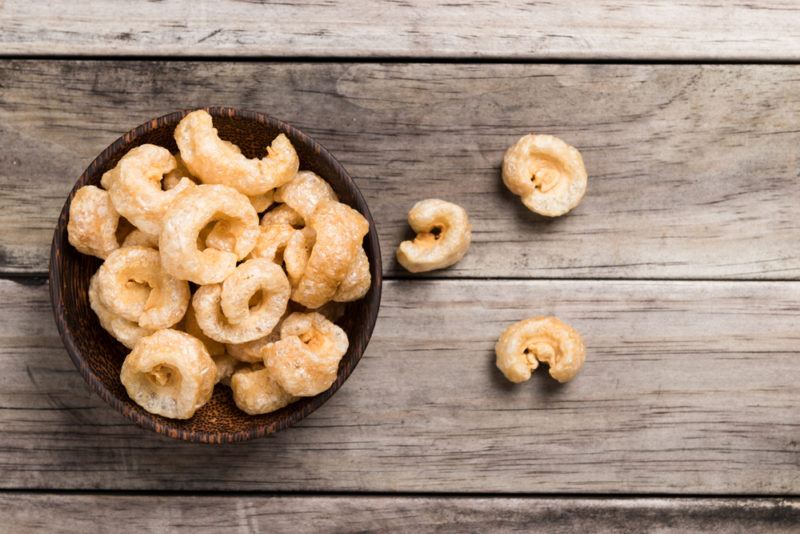 A black bowl of pork rines with three pork rinds on the table