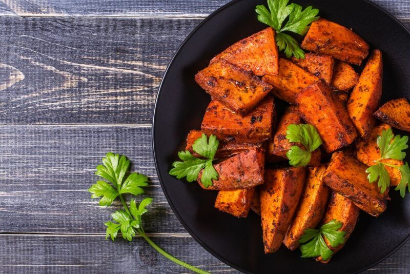 A black bowl filled with roasted sweet potatoes and some greens, on a wooden table