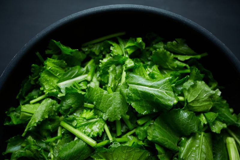 A black bowl filled with bright green turnip greens