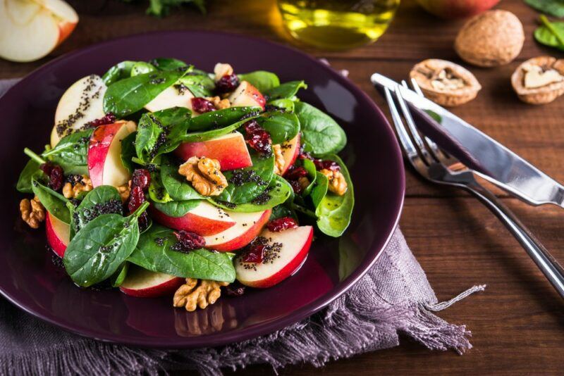 A black bowl with an apple and walnut salad next to a knife and fork