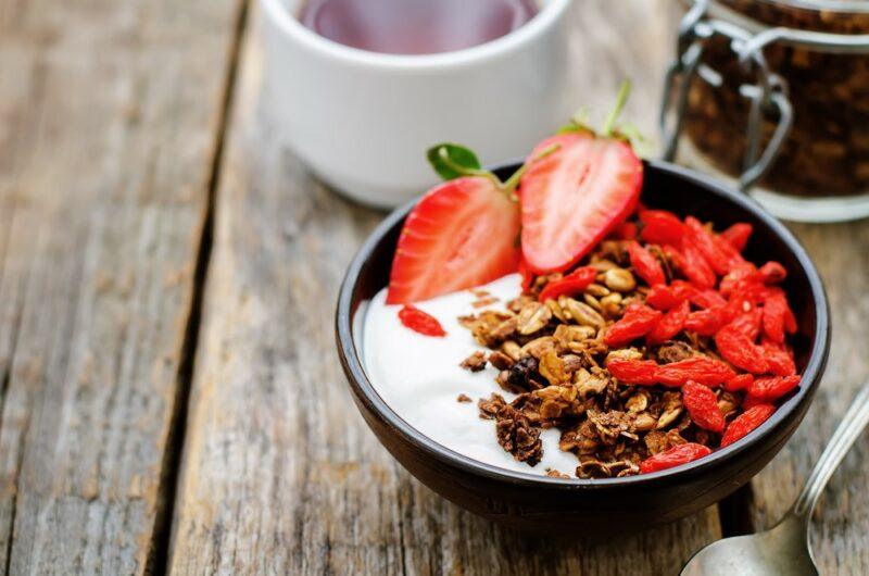 A dark bowl filled with cereal, yogurt, strawberries, and yogurt