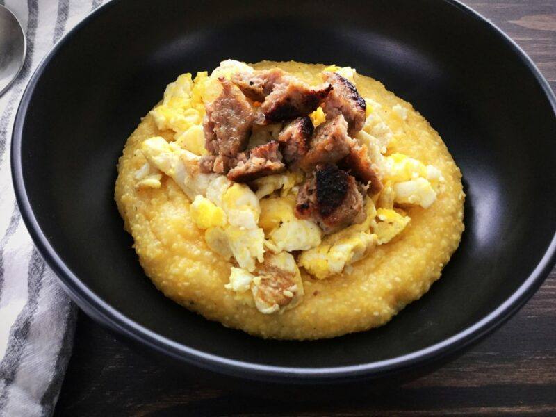 A black bowl with cooked grits, some meat, and other ingredients