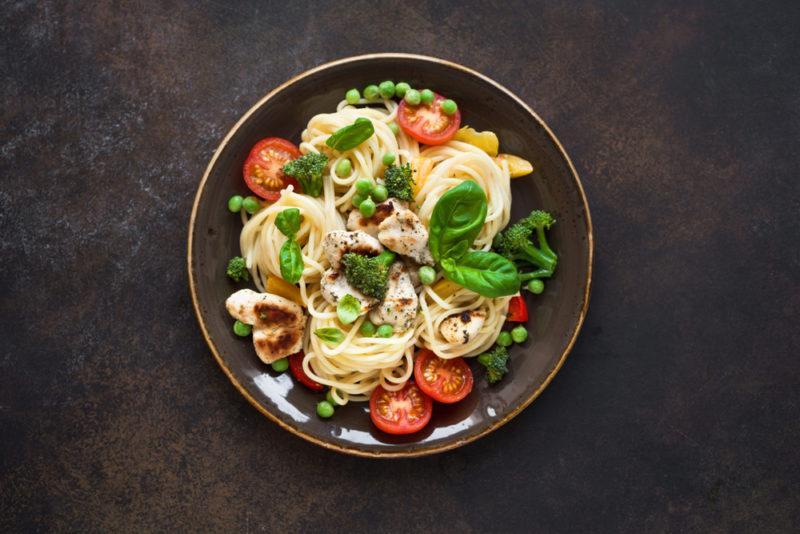 A black bowl containing pasta primavera that contains cherry tomatoes