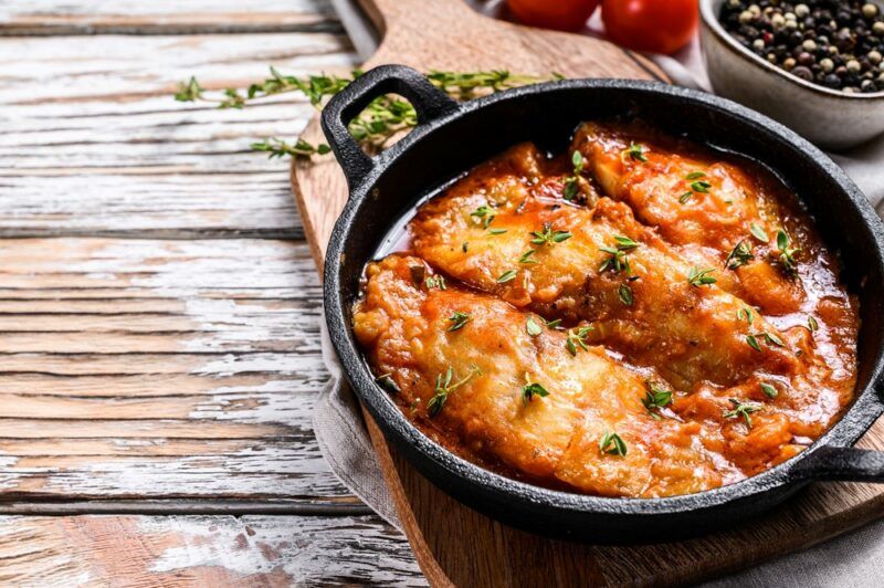 A black cast iron pan containing cooked tilapia on a wooden table