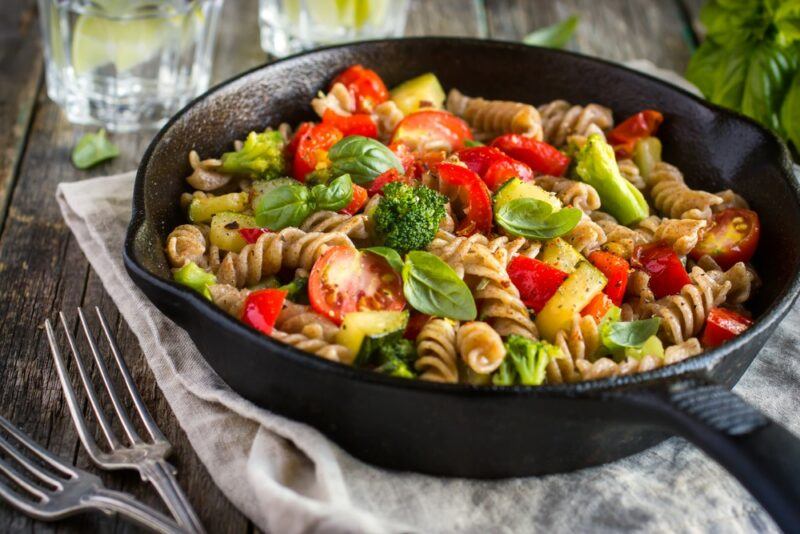 A black cast iron frypan with tomatoes and pasta, next to some forks