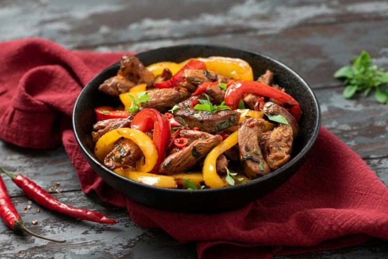 A table with a black dish containing meat and hot peppers