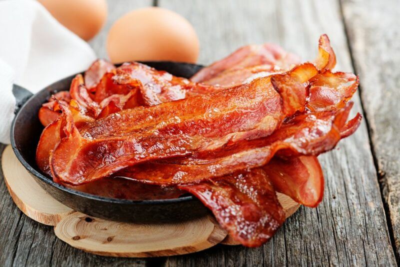 A black dish containing cooked bacon, with eggs behind it